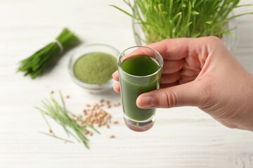 Woman holding glass of wheat grass drink at white table, closeup