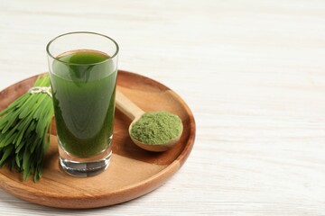 Wheat grass drink in shot glass, spoon of green powder and fresh sprouts on white wooden table,...