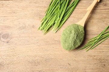 Wheat grass powder in spoon and fresh green sprouts on wooden table, flat lay. Space for text