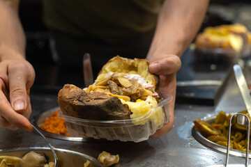 Turkish street food Kumpir. Male cook adds different fillings to the Kumpir. Delicious baked potatoes with a variety of mixed fillings