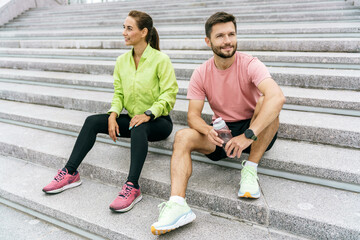 couple enjoys a restful break on stone steps during their workout, equipped with water bottles and...