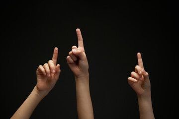 Three children's, teenager's hands pointing with index finger up against black background. Arms...