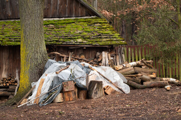 Logs of wood and chopped wood against the background of an old wooden building, village, retro. Stack of wood covered with foil.