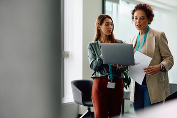 Female entrepreneurs cooperating while working on laptop in office.