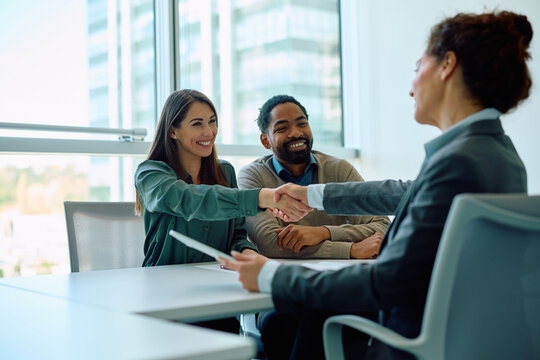 Happy couple handshaking with their financial advisor on meeting in office.