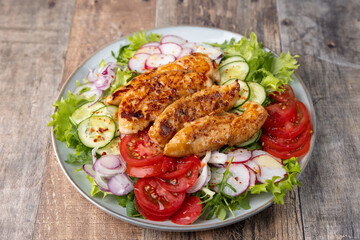 Warm salad with baked chicken breast and fresh vegetables, dressed with olive oil on a wooden background. Home kitchen in rustic style. Hearty delicious food. Selective focus, close-up.