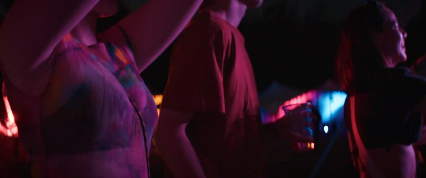 A diverse group of young people dance and laugh while enjoying live music at an outdoor festival at night
