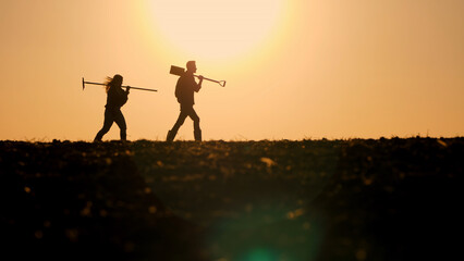 Silhouettes of two farmers walking with working tools across a field against the backdrop of a...