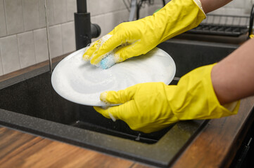 Myć naczynia, szorować brudny talerz w rękawicach do zmywania