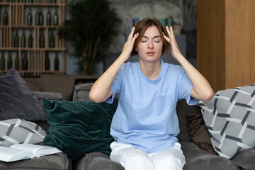 Young attractive woman with headache sitting on the couch at home	