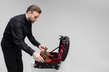 Bearded man artist packing musical instrument in violin case