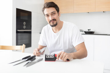 Close-up photo of man sharpening knives with special knife sharpener at home	