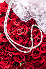 Wedding composition for the design of a postcard, cover, invitation. Pearl beads, two gold rings against a background of gorgeous red roses. Top view.