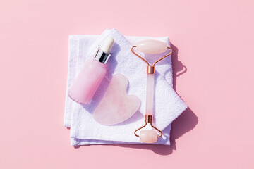 Roller massager, gua sha scraper, natural massage oil in a bottle with a dropper on a white towel. pink background. Health and beauty concept