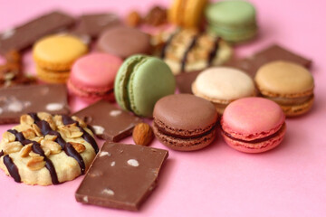 Pastel macarons, almond chocolate, peanut butter cookies and various nuts on bright pink background. Selective focus.