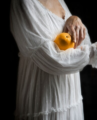 woman in white romantic style dress holding an orange in her arms V