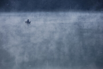Fototapeta premium barque avec pêcheurs dans la brume matinale sur le lac Genin dans l'Ain