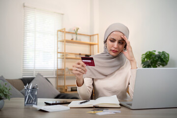 Credit card problem. Worried and stress young muslim woman in hijab sitting in living room working...