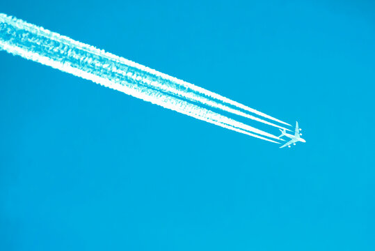 An airplane with four clear lines of contrails against a cloudless sky, the grace of flight. Travel symbol. technological progress, air pollution by chemical sprays from the air