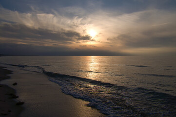 Sunset, illuminated sea. Sandy beach in the foreground. Light waves. Baltic Sea