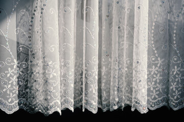 Sheer lace white pleated curtain tulle with embroidery and sequins in the rays of the sun