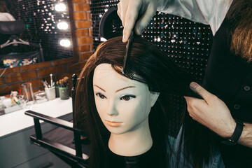 Hairdresser combing practice on mannequin .Man young hairdresser diligently enthusiastically with long beard and hair in vest ,combing hair hairstyle practicing on mannequin in beauty salon .concept