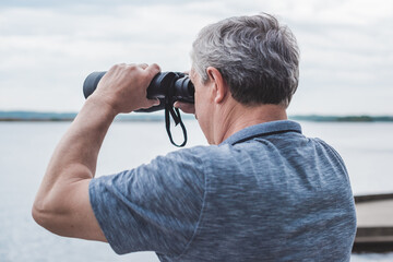 European Mature man looking in a binoculars . Hobby and recreation concept