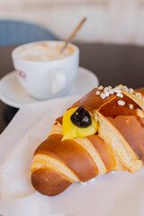 Cornetto artigianale ripieno di crema pasticciera e amarena servito in un bar per colazione accompagnato da un cappuccino caldo