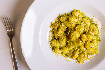 Gnocchi di patate con pesto di basilico, granella di pistacchio e formaggio grattugiato serviti in un ristorante elegante come primo piatto 