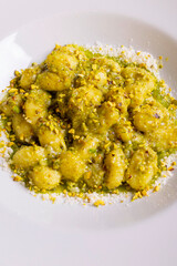 Gnocchi di patate con pesto di basilico, granella di pistacchio e formaggio grattugiato serviti in un ristorante elegante come primo piatto 