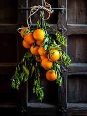 Bouquet of orange tree twigs with withered leaves and ripe oranges tied with a ribbon to a wooden door, marking orange season in a traditional and inviting display of Spanish culture and home decor.