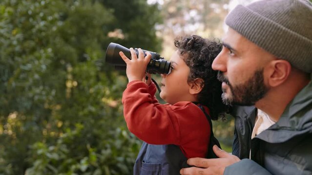 Curious child held by father using binoculars to explore nature, portraying learning, guidance, and a shared hobby in an outdoor setting in forest