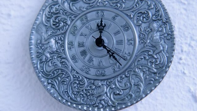vintage silver clock of 19th century on white wall counts down the time, the hands move on dial, concept of road of life, time goes by, an irreversible flow from past, through present to future
