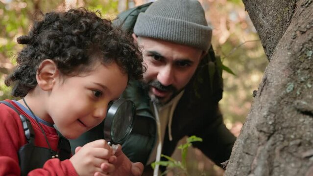Curious child explores nature using a magnifying glass, guided by an attentive father. A delightful family outdoor activity fostering learning and discovery.