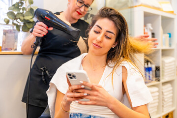 Client using phone while hairdresser drying her hair