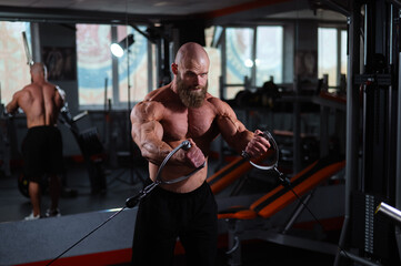 Bald Caucasian bodybuilder training chest using cable crossover in gym. 