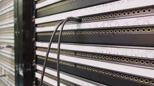 Patch panel in broadcast center, black SDI cable connected into BNC jack of back commutation panel of telecommunication video switcher with lot of jacks in broadcast technical room of TV channel