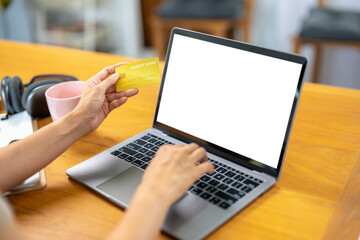 A woman is using a laptop to pay for something with a credit card. The laptop screen is blank, and...