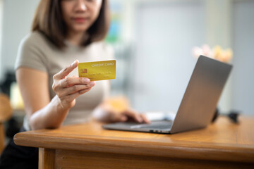 A woman is holding a credit card in front of a laptop. She is likely using the card to make a...
