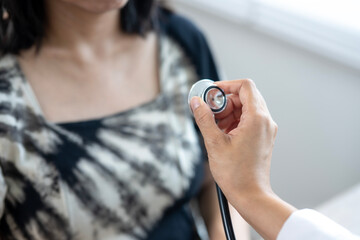 A doctor is examining a woman with a stethoscope. The woman is wearing a black and white shirt