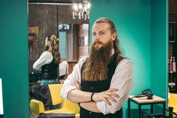 Man Bearded barber portrait .Male european young barber barber cheerful bearded long haired, standing with haircutting scissors in cookies and smiling in beauty salon hairdresser, portrait .Concept