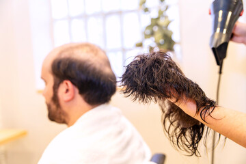 Bald man waiting while hairdresser drying his capillary prosthesis