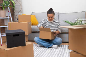 Moving Forward: Young woman in new home, surrounded by carton boxes, unpacks her world,...