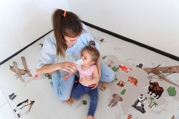 A woman is happily feeding a baby with a bottle, sitting on the floor. They are sharing a special moment, filled with smiles and laughter, enjoying leisure time together