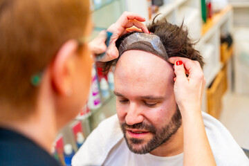 Hairdresser attaching a capillary prosthesis carefully to a man's head
