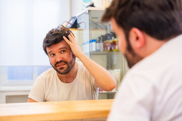 Bald man with capillary prosthesis looking into hair salon mirror