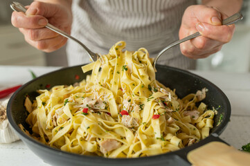 Preparing pasta pan aglio e olio with chicken breast by womans hands