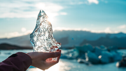 Hand holds a large piece of ice. Frozen water melts in the sun. Light reflections, sunset, melting...