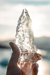 Hand holds a large piece of ice. Frozen water melts in the sun. Light reflections, sunset, melting...