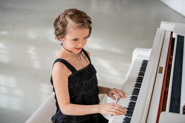 A young girl is playing the piano in a black dress.